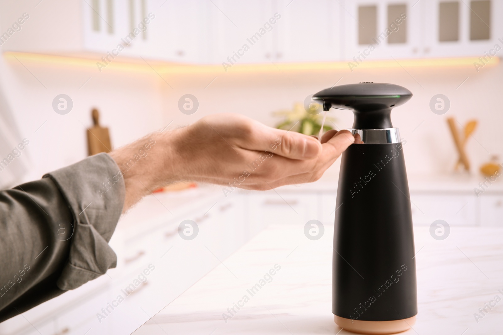 Photo of Man using automatic soap dispenser in kitchen, closeup