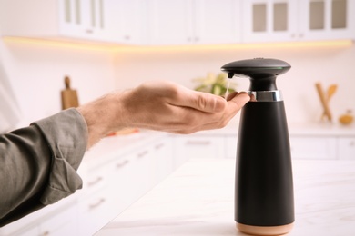 Photo of Man using automatic soap dispenser in kitchen, closeup