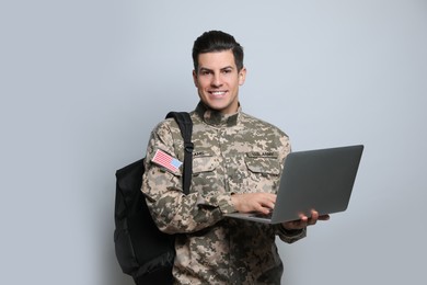 Photo of Cadet with backpack and laptop on light grey background. Military education