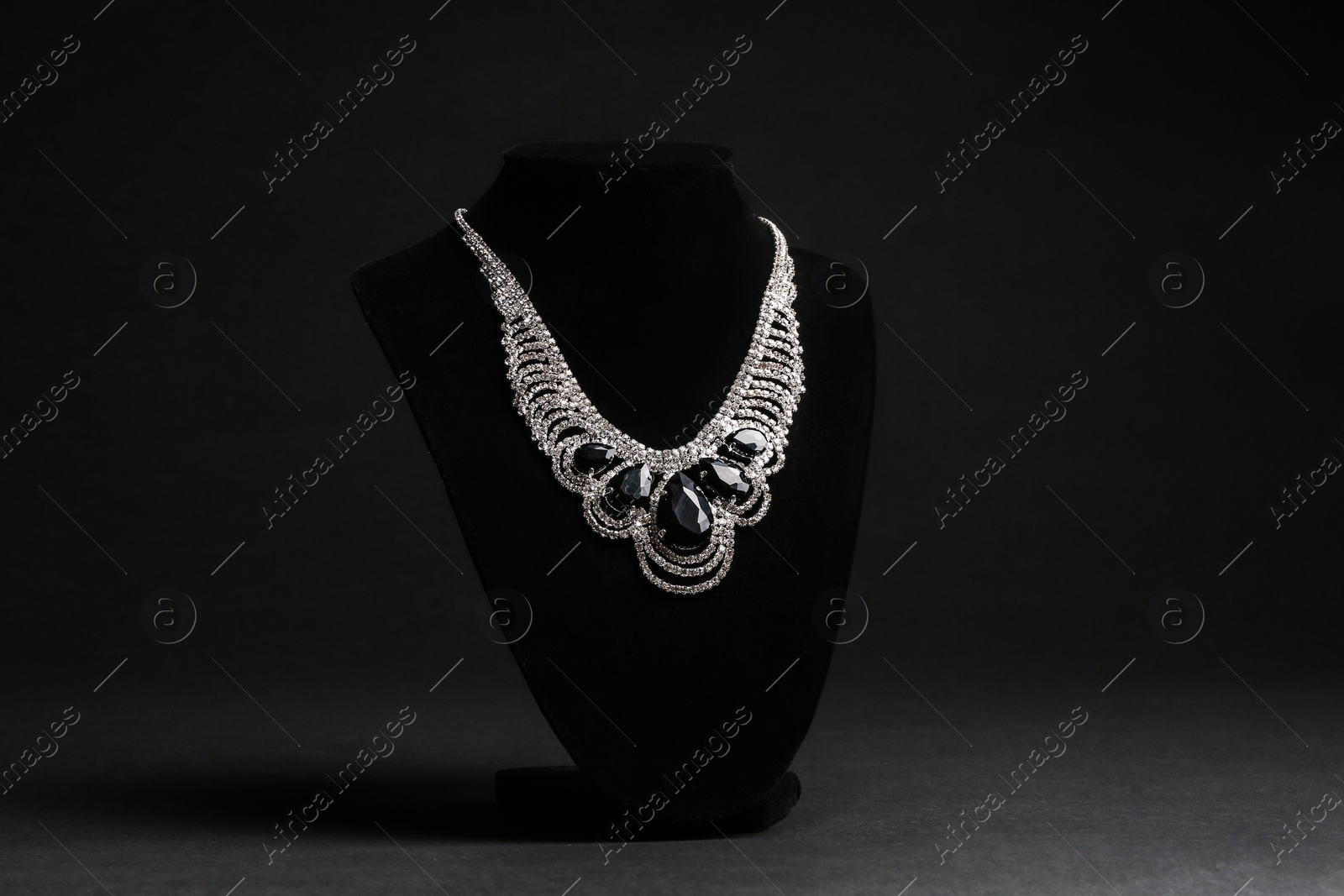 Photo of Elegant necklace on stand against black background. Luxury jewelry