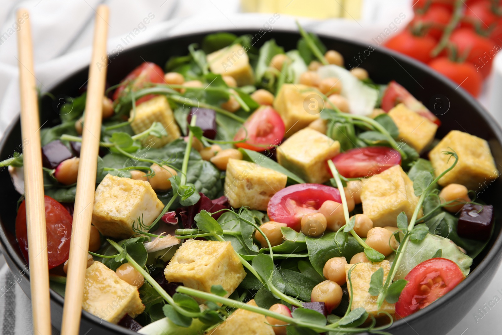 Photo of Bowl of tasty salad with tofu, chickpeas and vegetables on table, closeup