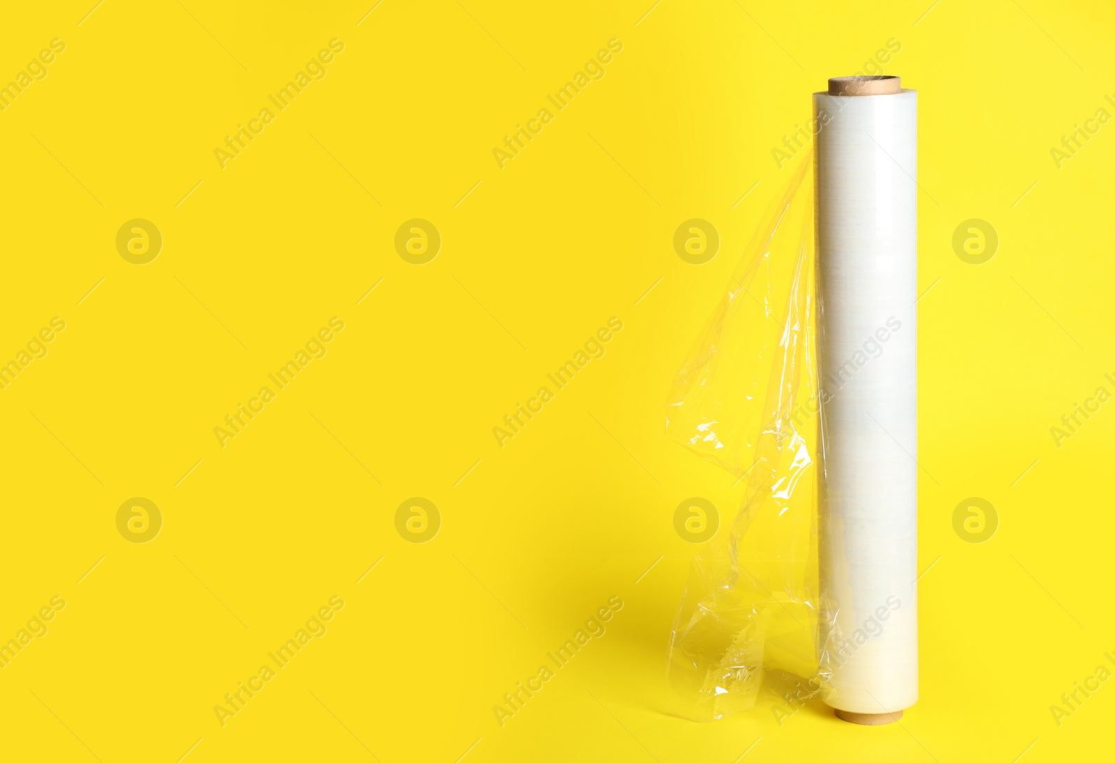 Photo of Roll of plastic stretch wrap film on yellow background, space for text