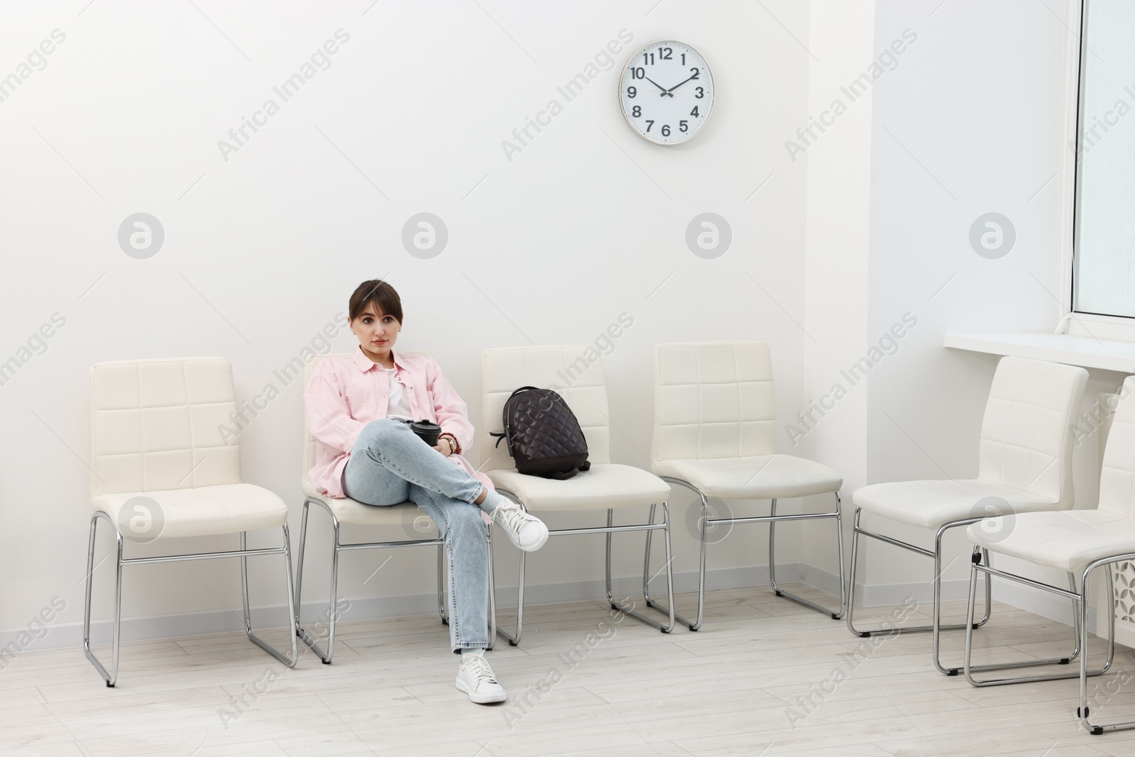 Photo of Woman with cup of drink waiting for appointment indoors