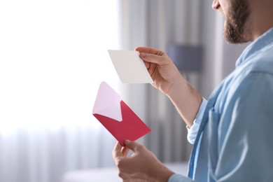 Photo of Man holding envelope and greeting card at home, closeup