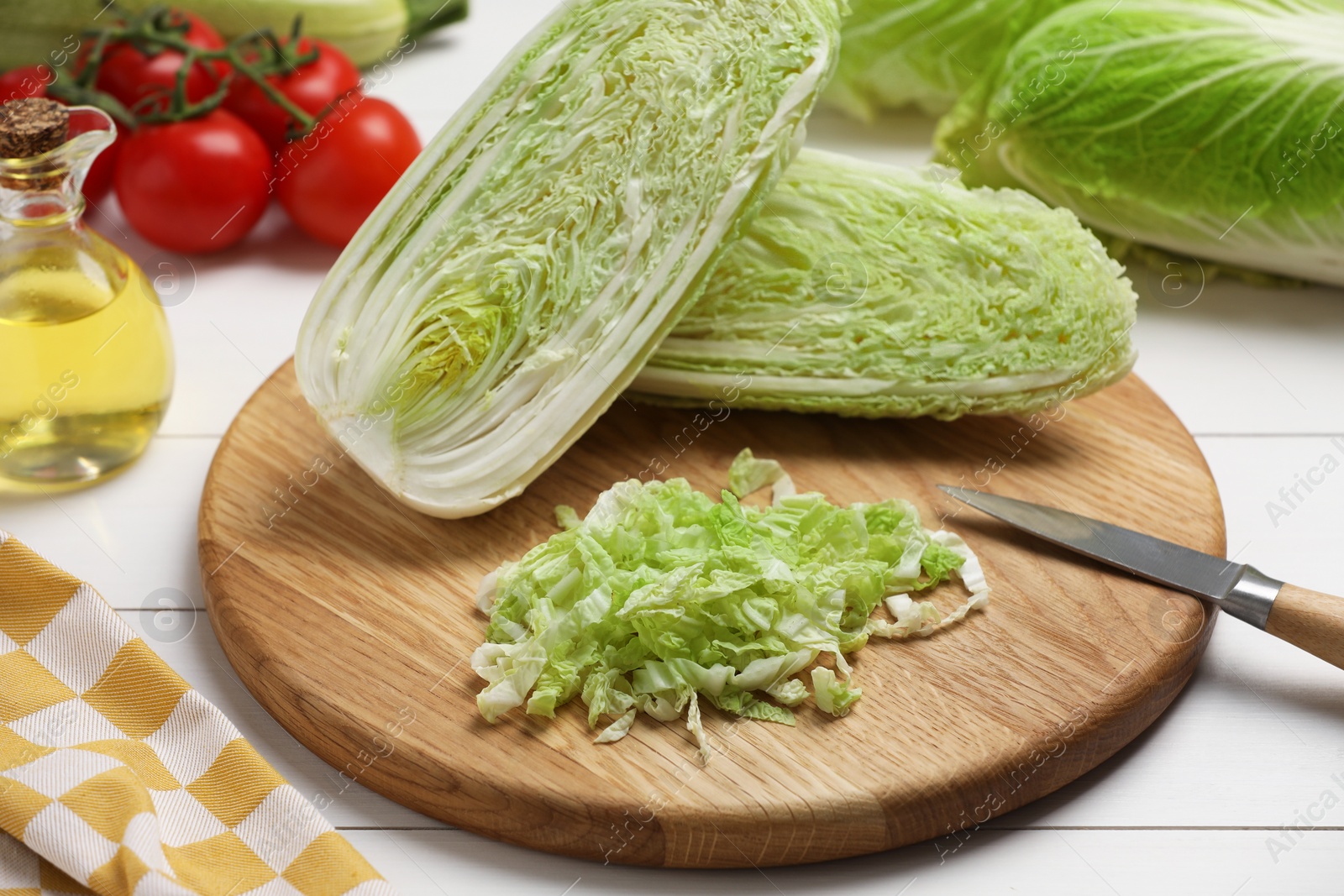 Photo of Fresh Chinese cabbages, knife, tomatoes and oil on white wooden table