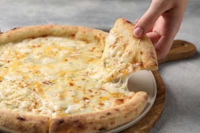 Photo of Woman taking piece of delicious cheese pizza at light grey table, closeup