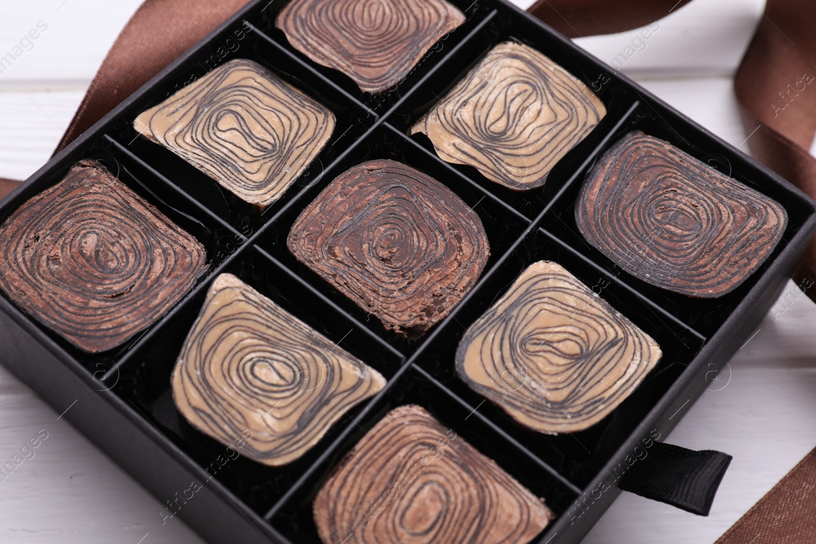 Photo of Box of tasty chocolate candies and ribbon on white wooden table, closeup