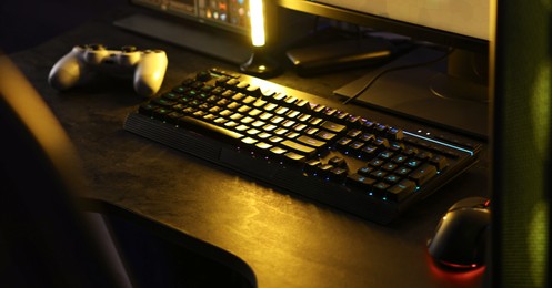 Playing video games. Computer monitor, keyboard, mouse and wireless controller on table indoors