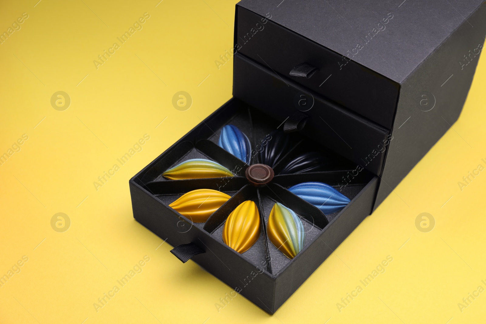 Photo of Box of tasty chocolate candies on yellow background