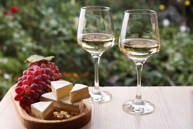 Glasses of white wine and snacks served on wooden table outdoors