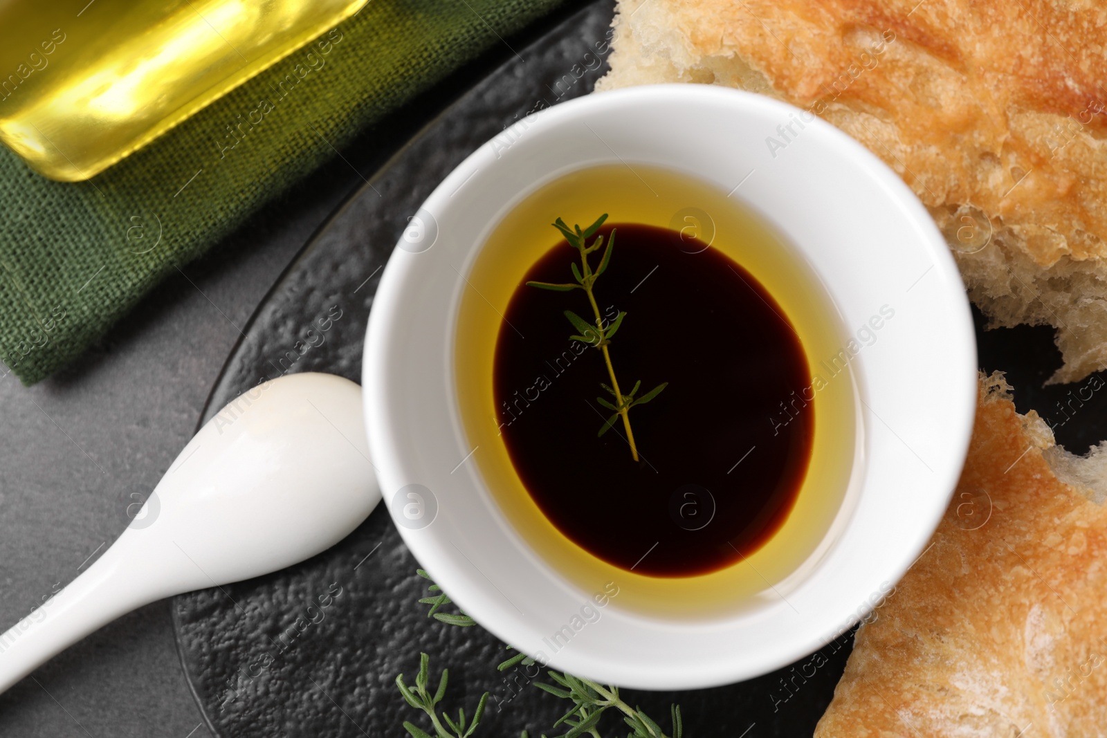 Photo of Bowl of organic balsamic vinegar with oil, thyme and bread on grey table, flat lay