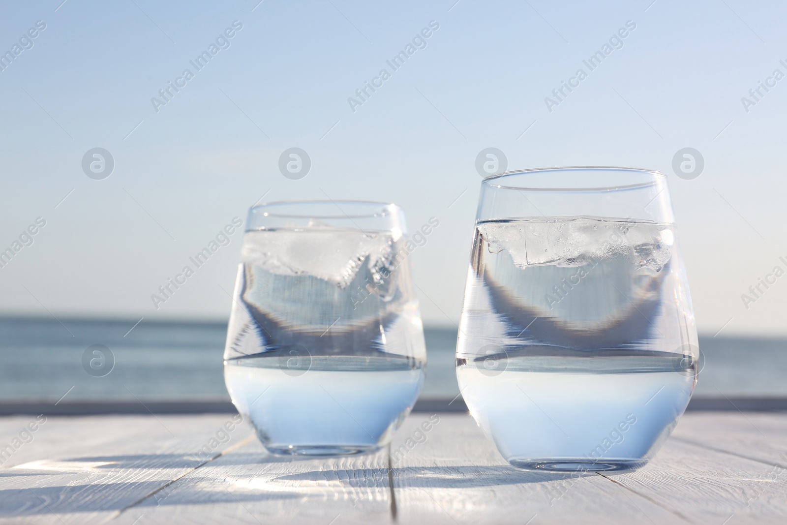 Photo of Wooden table with glasses of refreshing drink on hot summer day outdoors