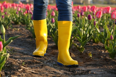 Photo of Woman in rubber boots walking across field with beautiful tulips after rain, closeup