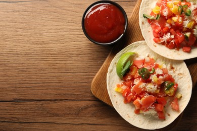 Photo of Delicious tacos with vegetables, lime and ketchup on wooden table, flat lay. Space for text