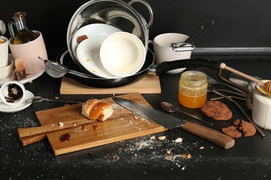 Many dirty utensils, dishware and food leftovers on black countertop. Mess in kitchen