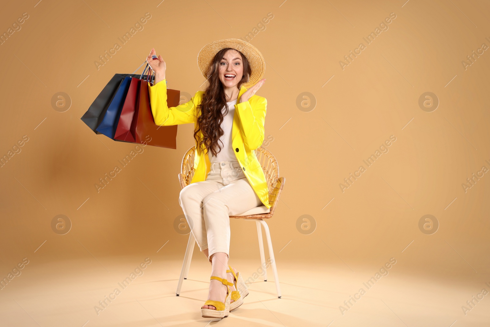 Photo of Emotional woman holding many colorful shopping bags on armchair against beige background