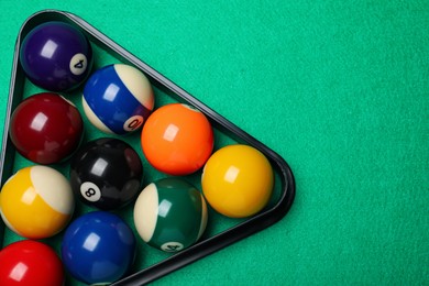 Plastic rack with billiard balls on green table, top view. Space for text