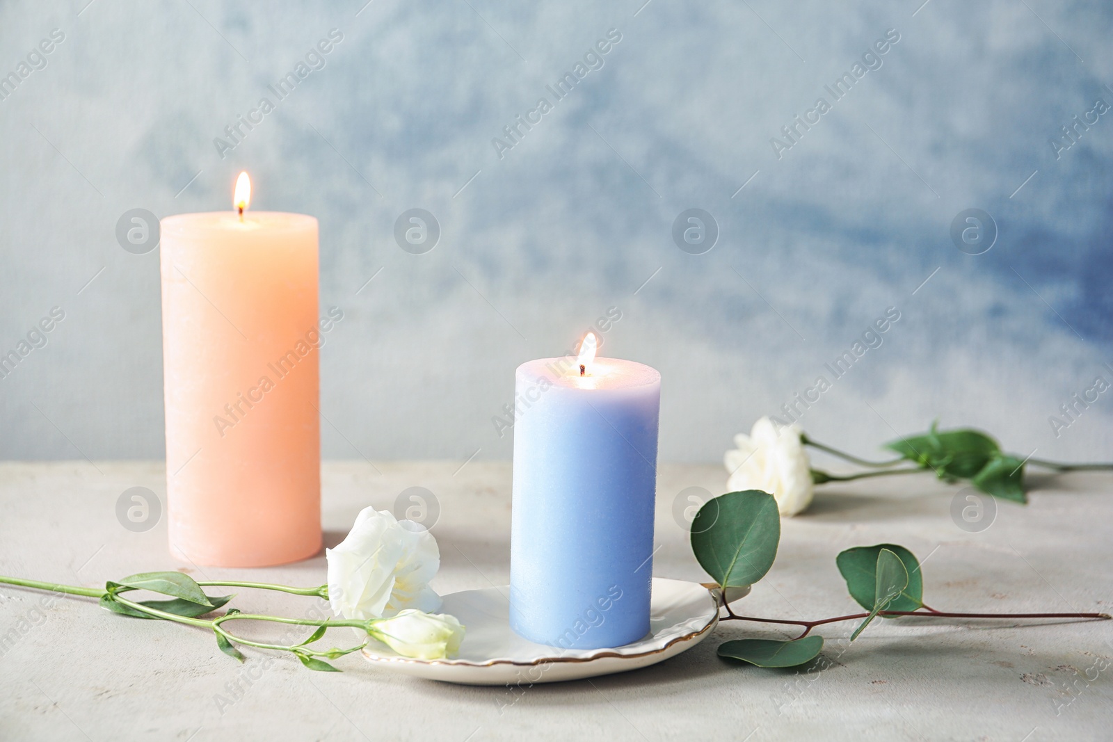 Photo of Candles with floral decor on table against color background