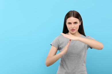 Photo of Woman showing time out gesture on light blue background, space for text
