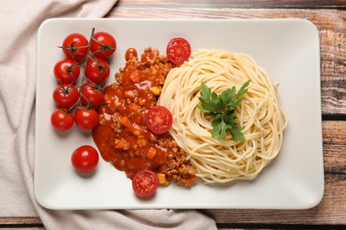 Photo of Tasty dish with fried minced meat, spaghetti, carrot, corn and cherry tomato served on wooden table, top view
