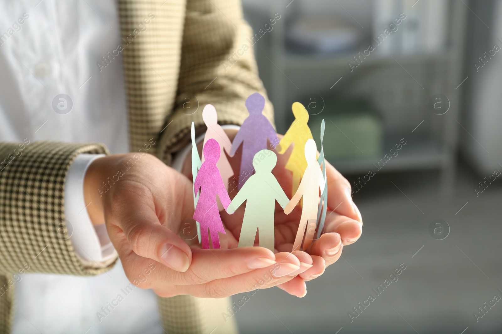 Photo of Woman holding paper human figures on blurred background, closeup. Diversity and inclusion concept