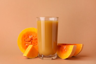 Photo of Tasty pumpkin juice in glass and cut pumpkin on pale orange background