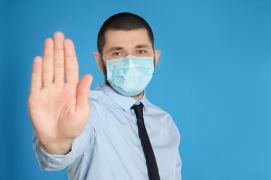 Photo of Man in protective mask showing stop gesture on light blue background, space for text. Prevent spreading of coronavirus
