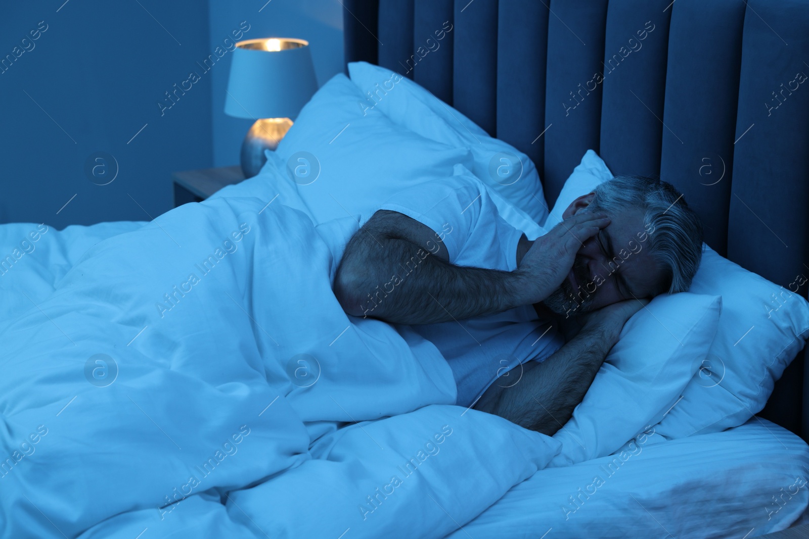 Photo of Mature man suffering from headache in bed at night