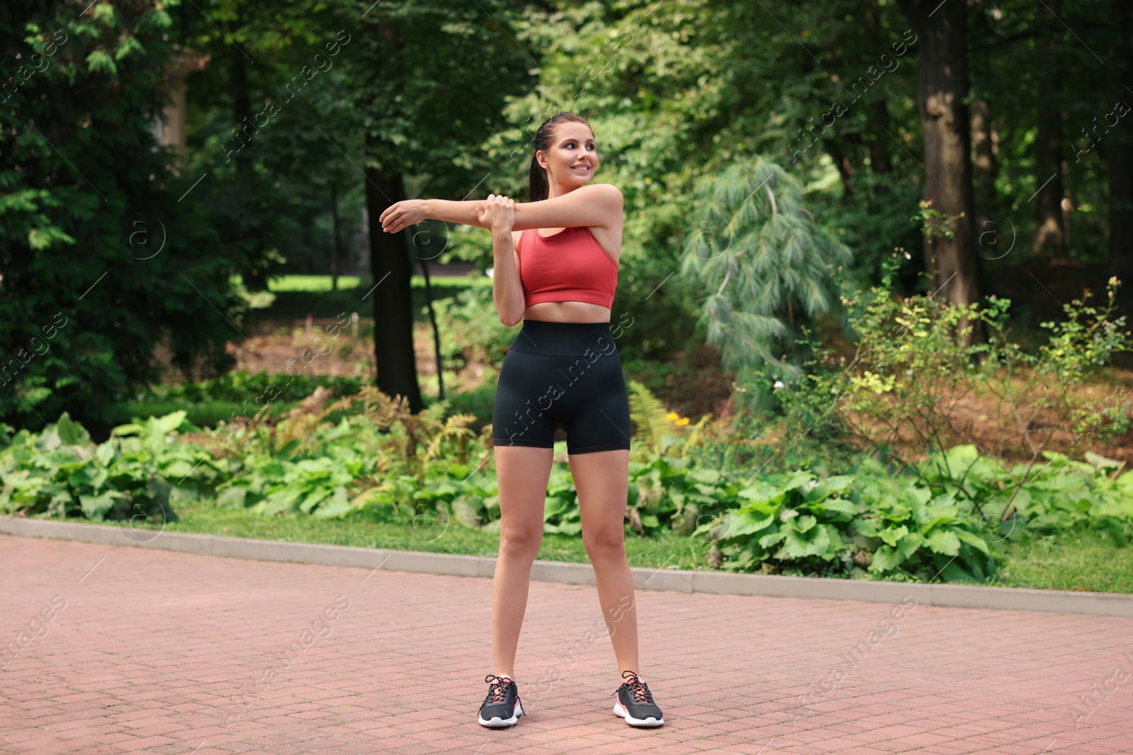 Photo of Smiling woman in sportswear stretching in park