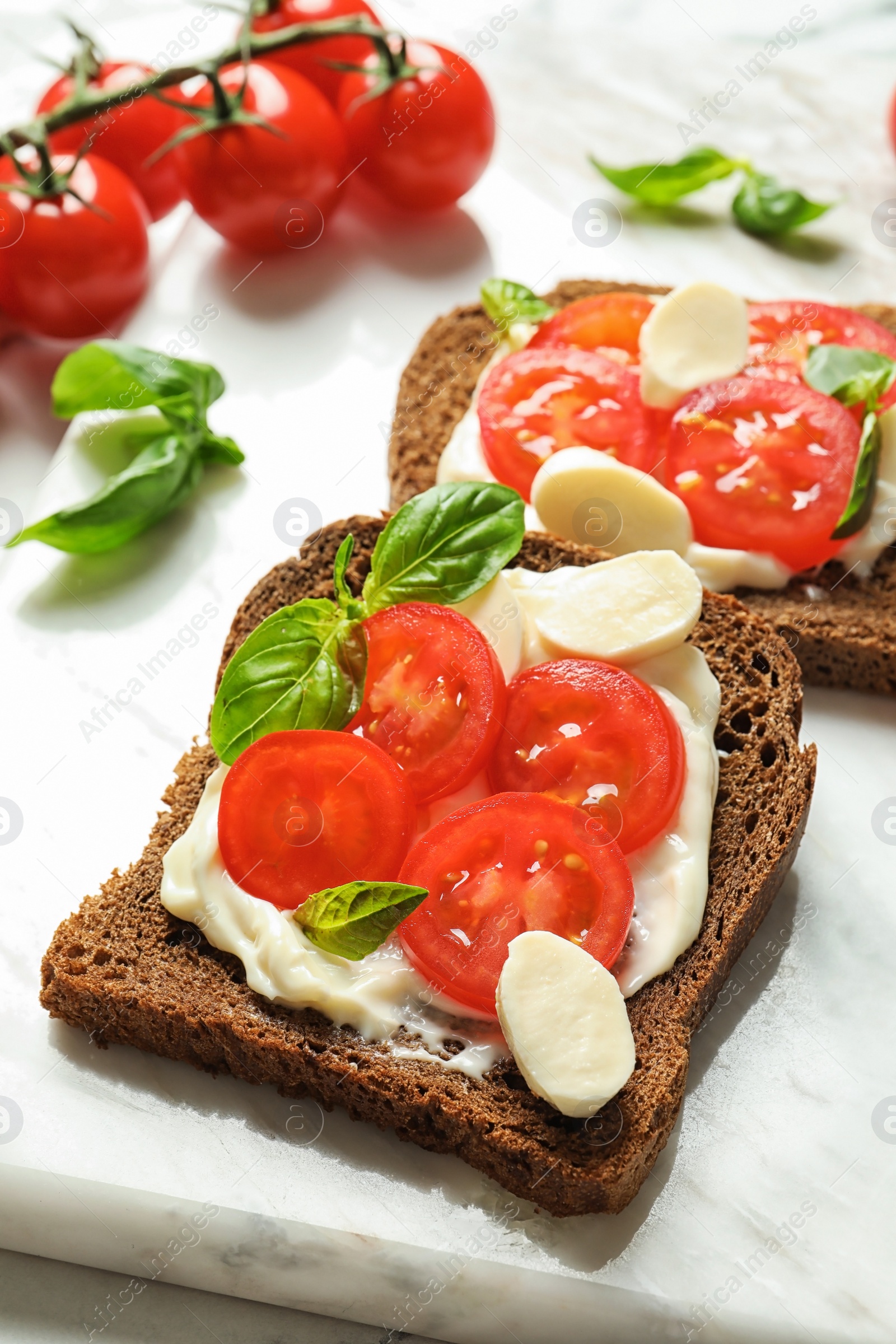 Photo of Toast bread with cherry tomatoes and mozzarella cheese on marble board, closeup