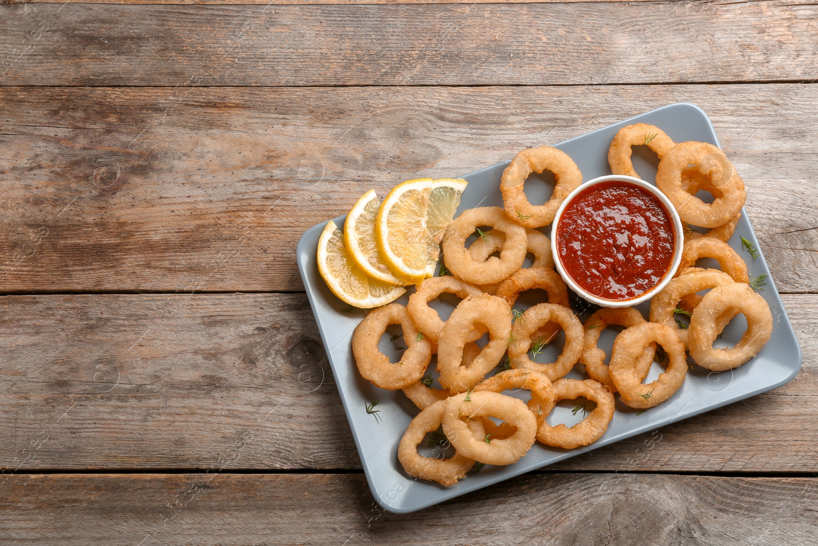 Photo of Fried onion rings served with sauce and lemon slices on plate, top view