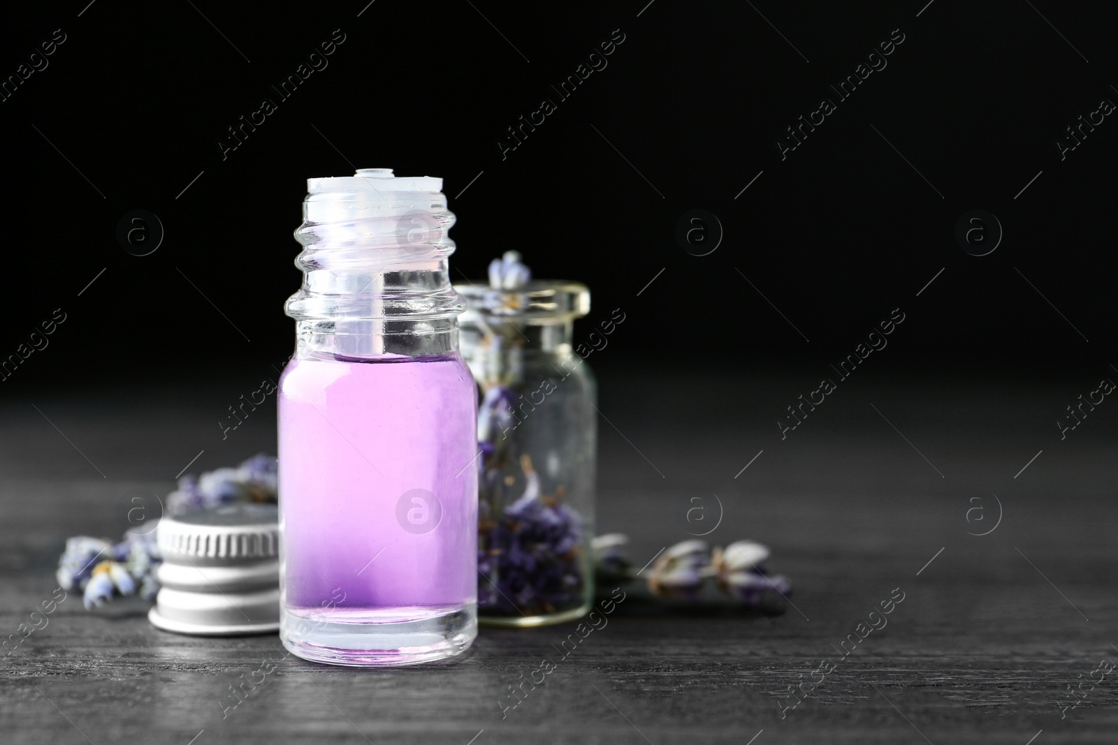 Photo of Bottles of natural essential oil and lavender flowers on dark wooden table. Space for text