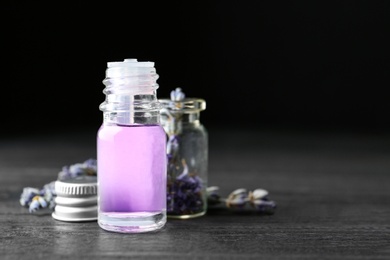 Photo of Bottles of natural essential oil and lavender flowers on dark wooden table. Space for text