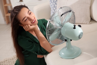 Woman enjoying air flow from fan at home. Summer heat