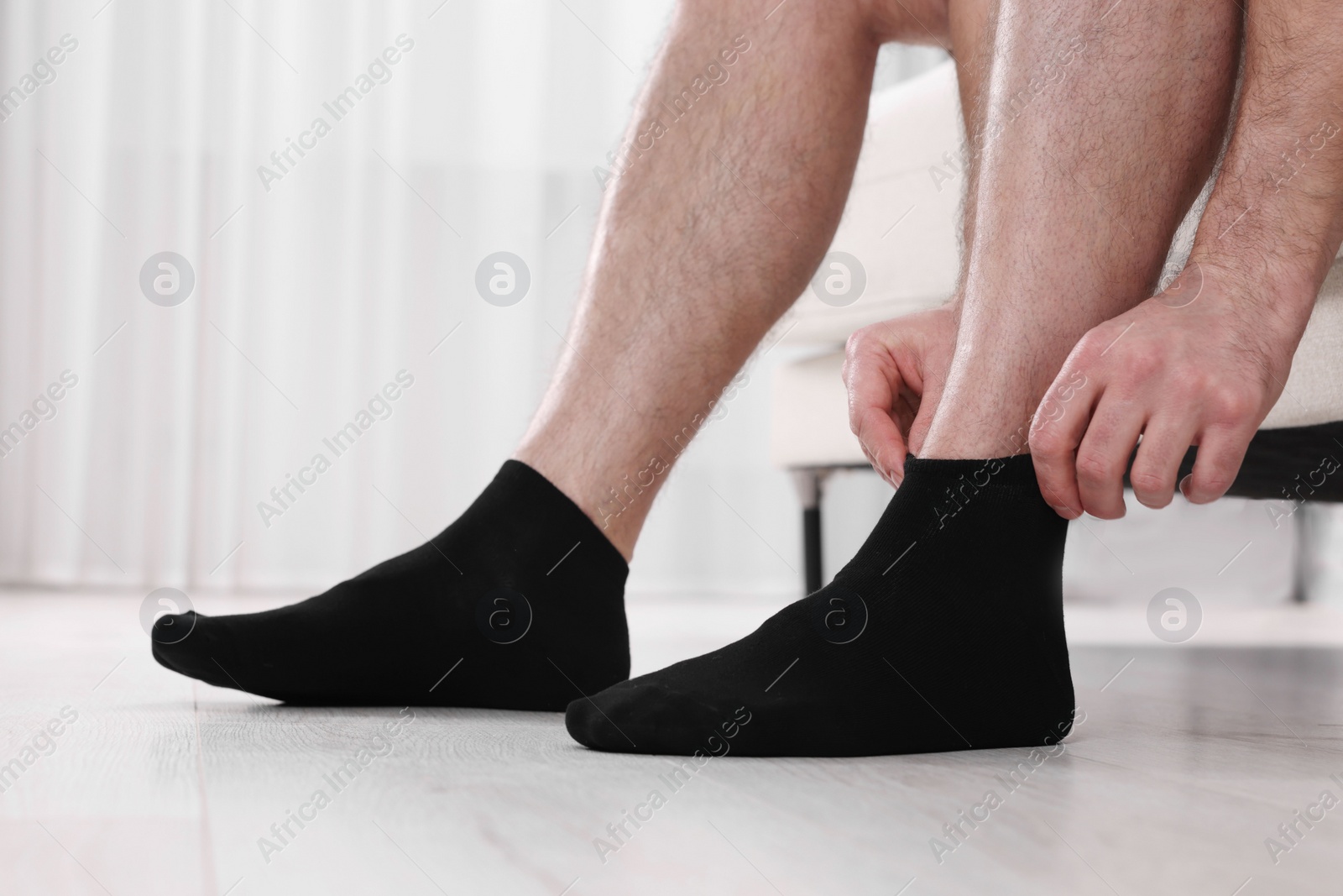 Photo of Man putting on black socks at home, closeup