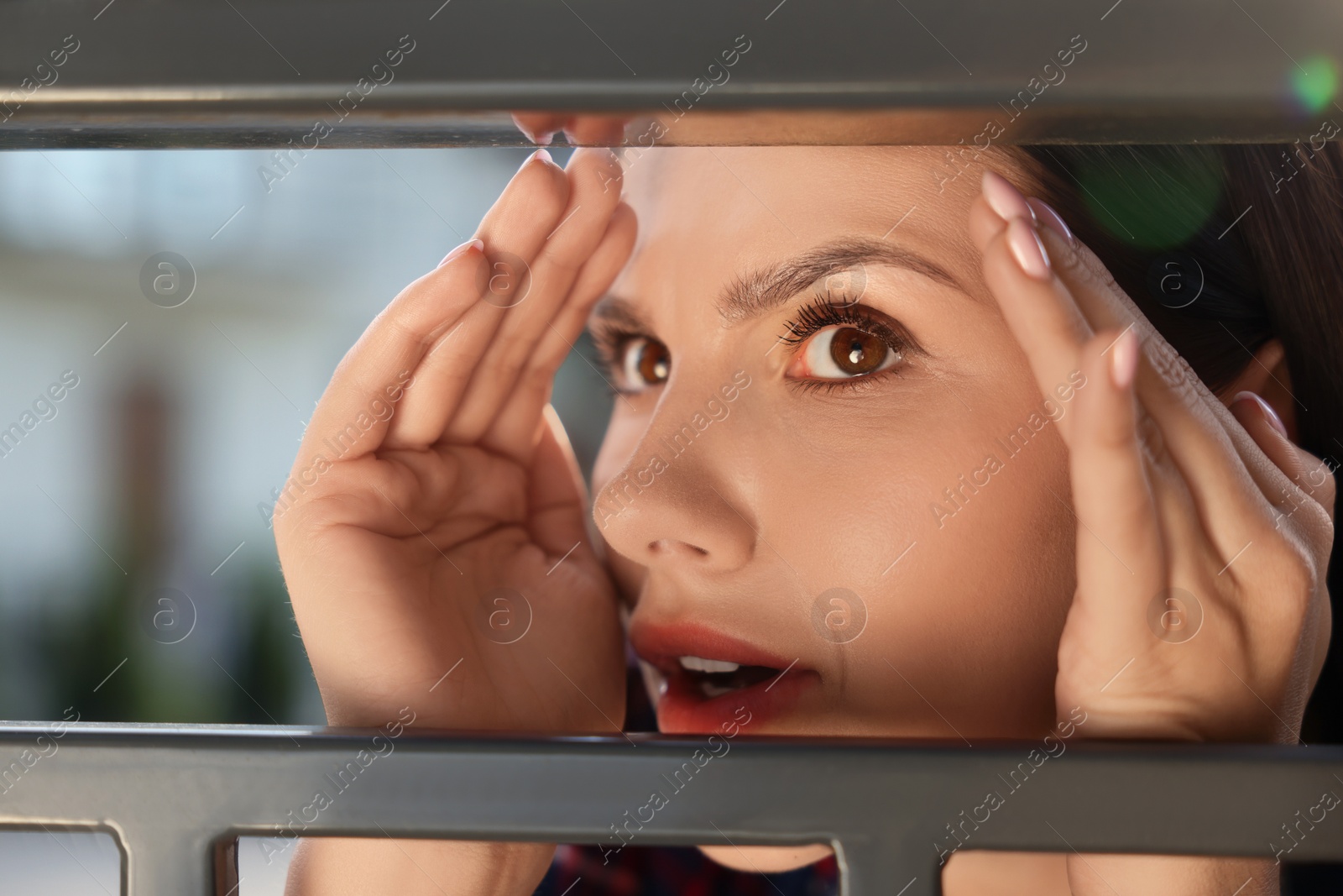 Photo of Concept of private life. Curious young woman spying on neighbours over fence outdoors, closeup