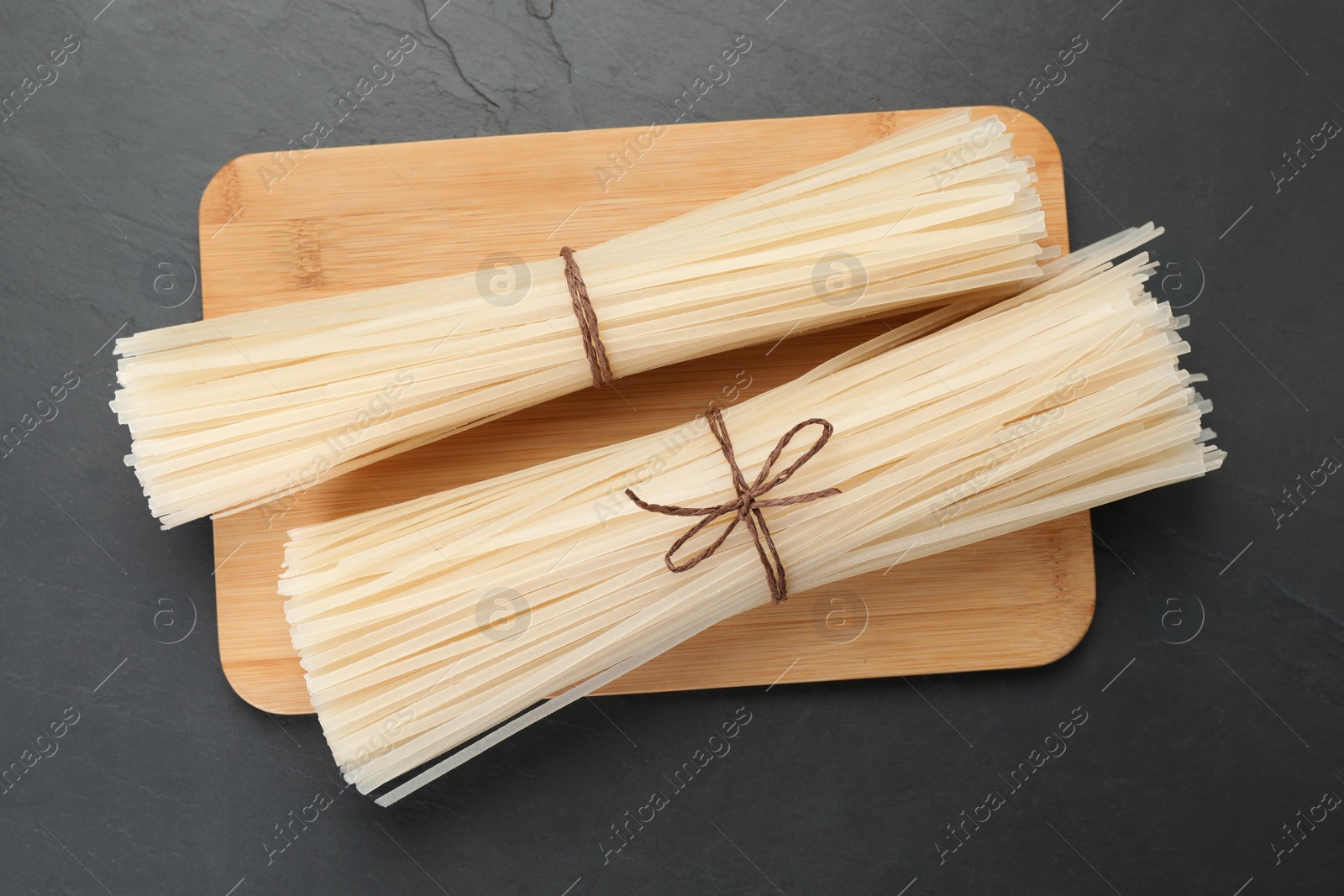 Photo of Dried rice noodles with wooden board on black table, top view
