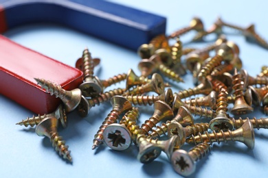 Photo of Magnet attracting screws on light blue background, closeup