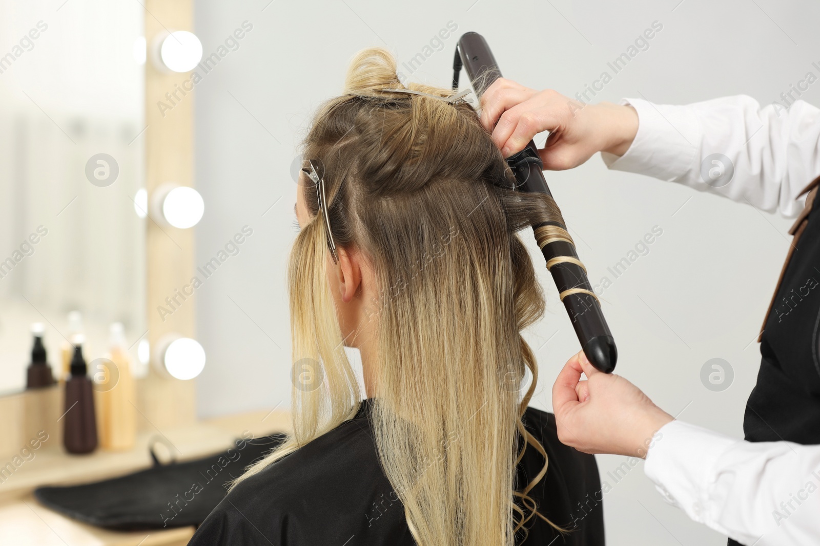 Photo of Hair styling. Hairdresser curling woman's hair in salon, closeup