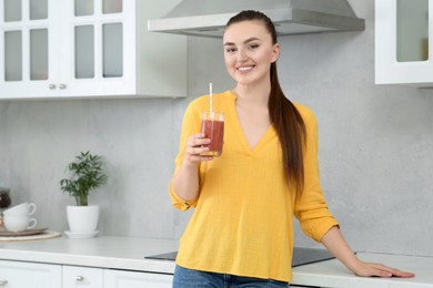 Photo of Beautiful young woman with delicious smoothie in kitchen. Space for text