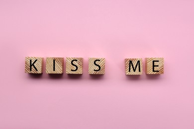 Photo of Wooden cubes with phrase Kiss Me on pink background, flat lay