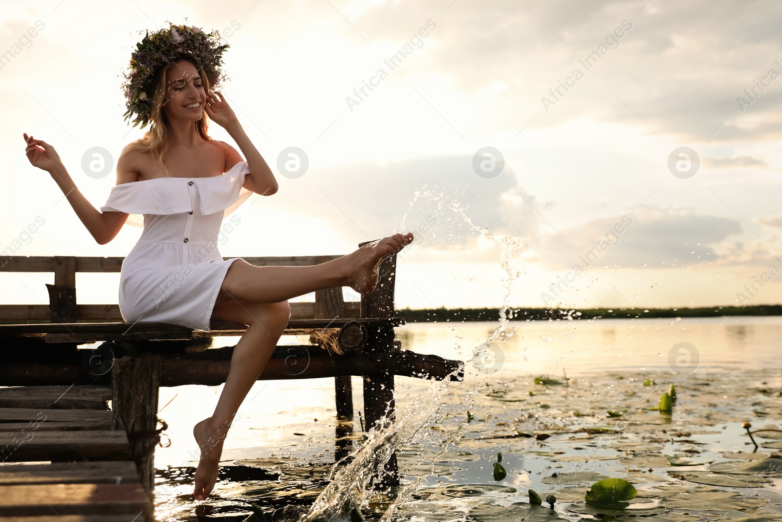 Photo of Young woman wearing wreath made of beautiful flowers on pier near river