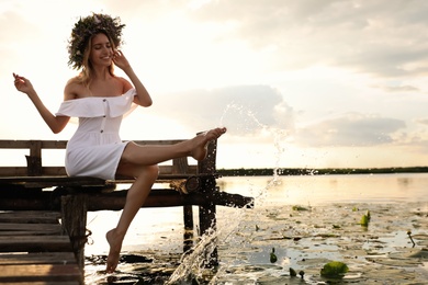 Young woman wearing wreath made of beautiful flowers on pier near river