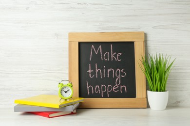 Photo of Small chalkboard with motivational quote Make Things Happen, notebooks, alarm clock and plant on white wooden table