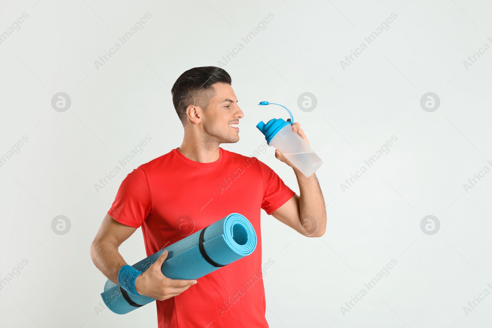 Photo of Handsome man with yoga mat drinking water on light background