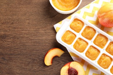 Photo of Nectarine puree in ice cube tray and fresh nectarine fruits on wooden table, flat lay. Space for text