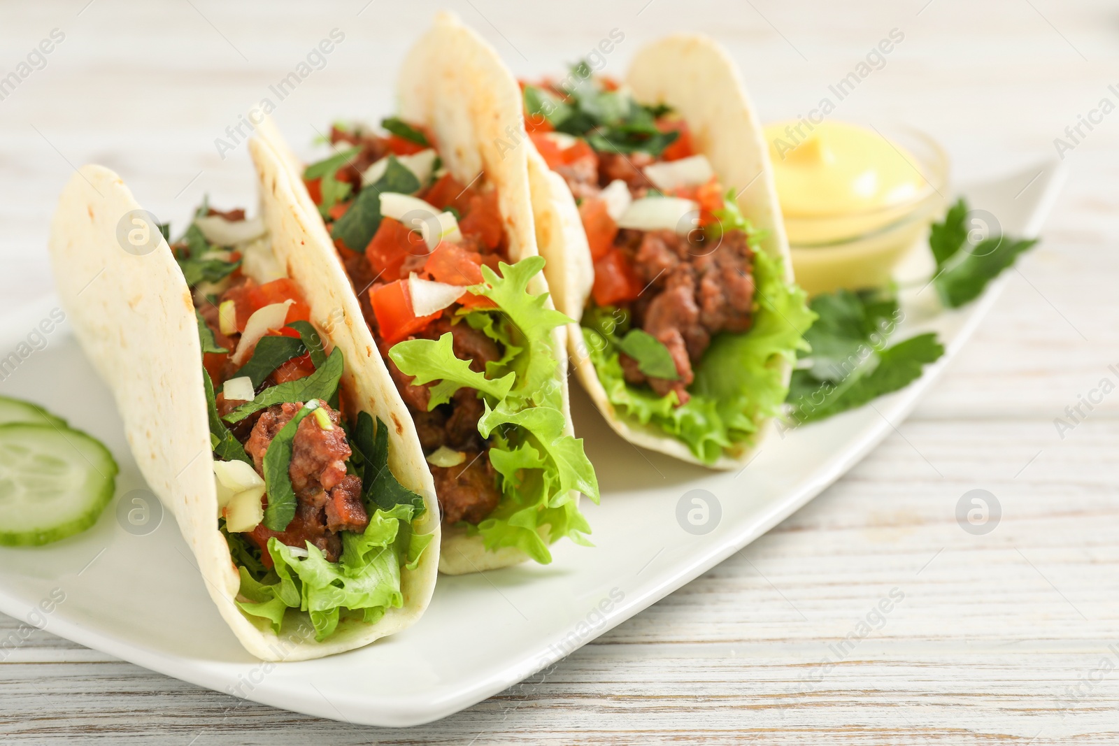 Photo of Delicious tacos with meat and vegetables on wooden table, closeup