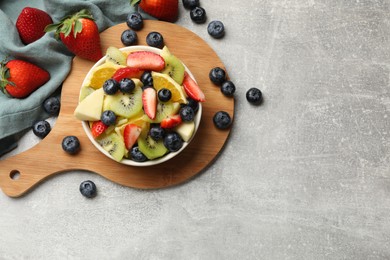 Photo of Tasty fruit salad in bowl and ingredients on gray textured table, flat lay. Space for text