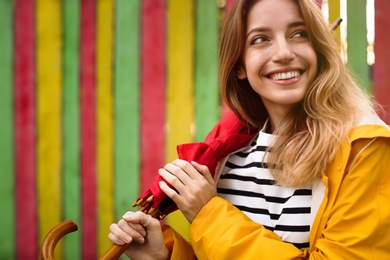 Photo of Beautiful young woman in stylish autumn clothes with red umbrella near color fence