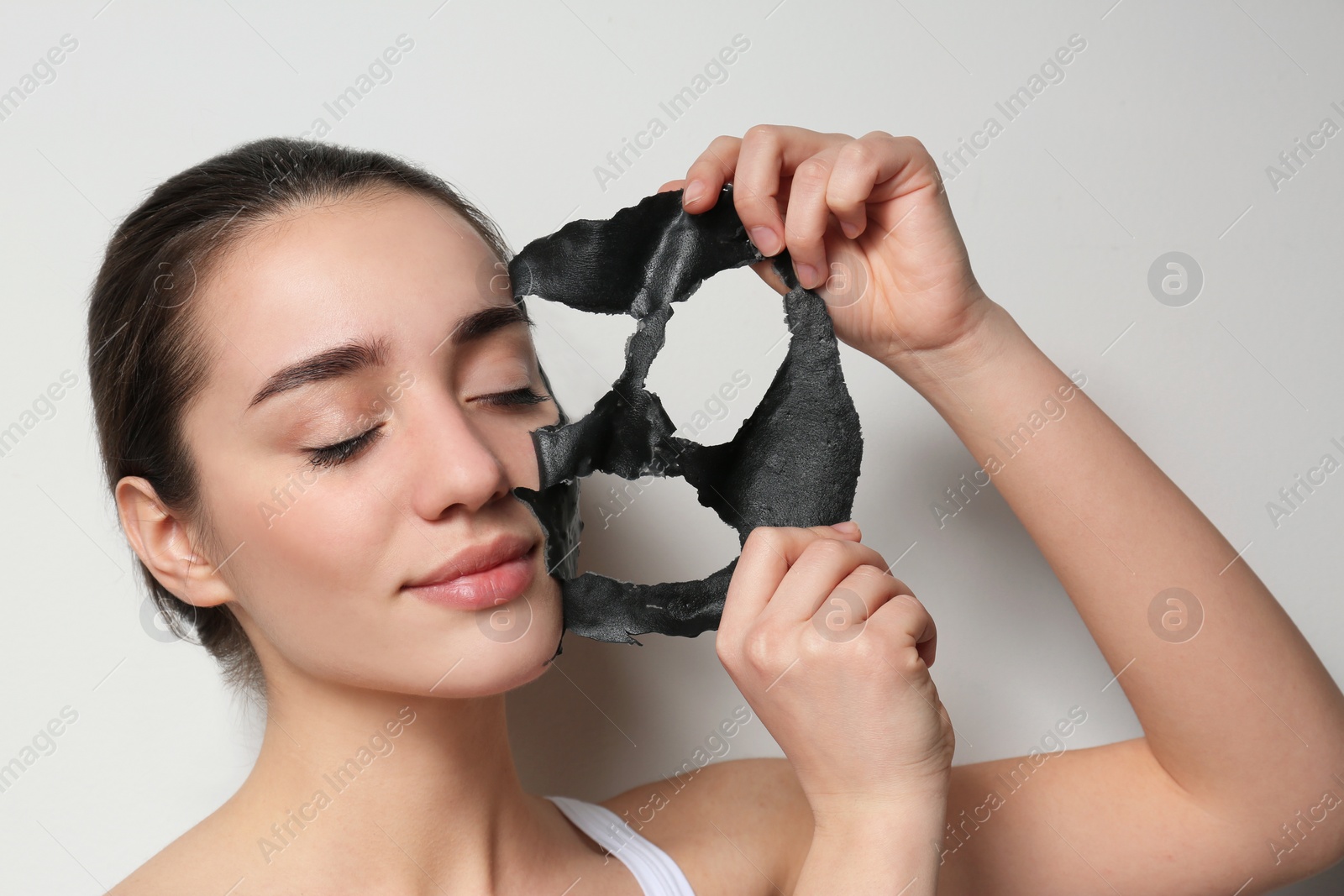 Photo of Beautiful young woman removing black mask from her face on white background